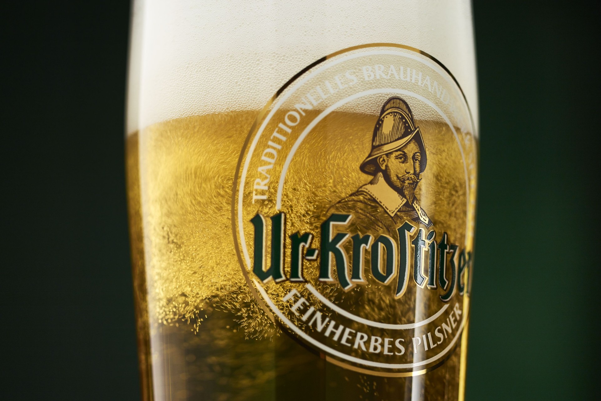 Ein Bierglas der Marke Ur-Krostitzer mit Bier gefüllt vor grünem Hintergrund