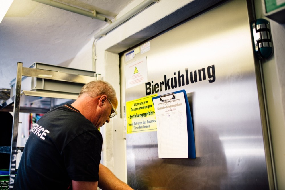 Ein Mann schreibt an einer Klemmmappe an einer metallischen Tür mit der Aufschrift Bierkühlung.