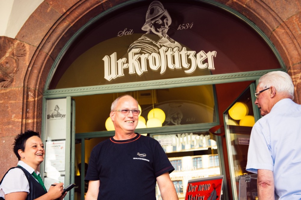 Drei Personen stehen lächelnd vor einem historischen Gasthaus.