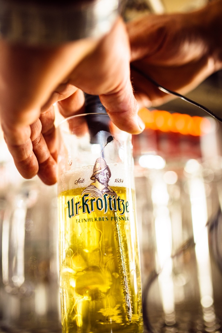 Eine Hand gießt Bier in ein Glas mit sichtbarem Markenlogo.