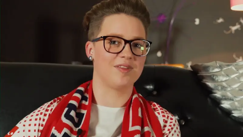 Person mit Brille und rotem Fanschal sitzt auf einem schwarzen Ledersessel.