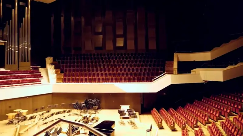 Großer Konzertsaal mit leeren roten Sitzreihen und Orgel. Auf der Bühne stehen Stühle und Musikinstrumente.