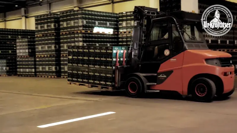 Gabelstapler transportiert Paletten mit grünen Ur-Krostitzer Bier-Getränkekisten in einer Lagerhalle.