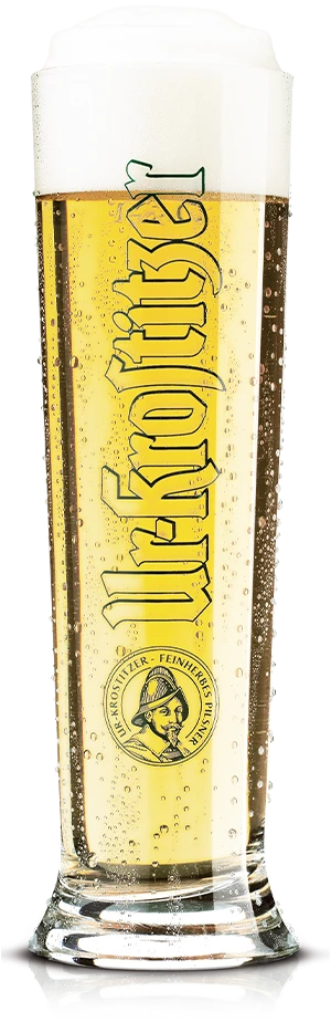 Ein volles Bierglas mit Schaumkrone steht auf einer klaren Oberfläche. Das Glas trägt eine Beschriftung in großen Buchstaben.