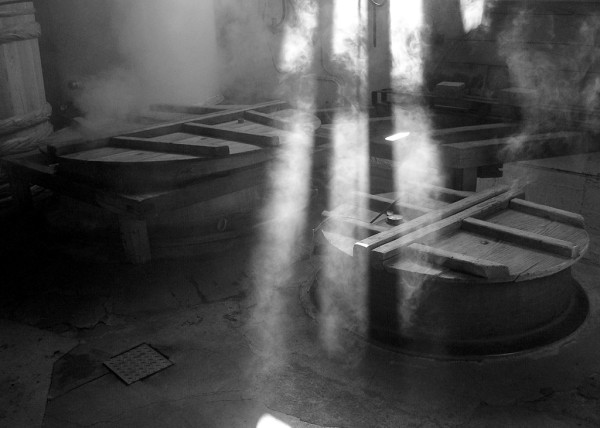 Holzfässer mit wirbelndem Dampf in einem dunklen Raum erzeugen eine geheimnisvolle Atmosphäre.