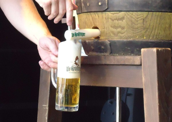 Ein Glas Bier wird aus einem Holzfass in einer dunklen Umgebung gezapft.
