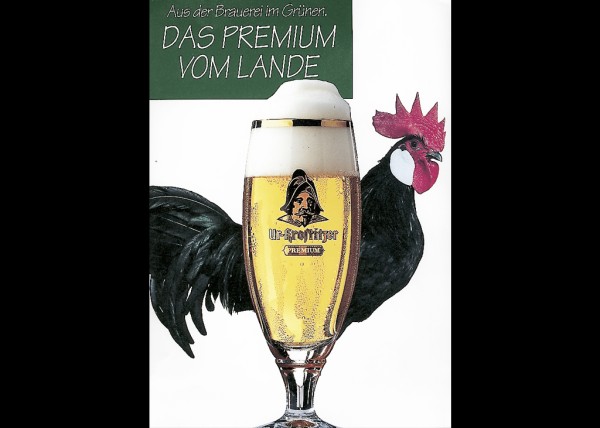 Ein gläsernes Bierglas mit aufgemaltem Hahn steht vor einem grünen Hintergrund.