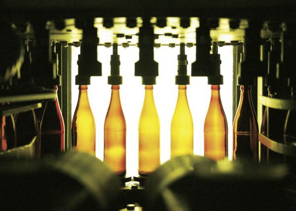 Mehrere beleuchtete, klare Flaschen stehen in einer Abfüllanlage auf einem Förderband.