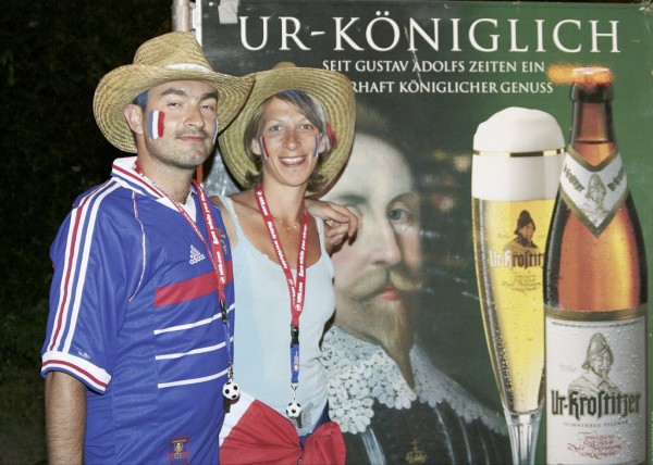 Zwei Personen in Freizeitkleidung stehen lächelnd vor einem Werbeplakat.