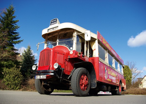 Ein roter, historischer Bus steht auf einer Straße vor einem blauen Himmel.