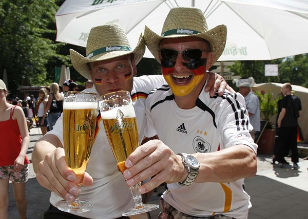 Zwei Männer mit Strohhüten und bemalten Gesichtern in den deutschen Farben halten Biergläser.