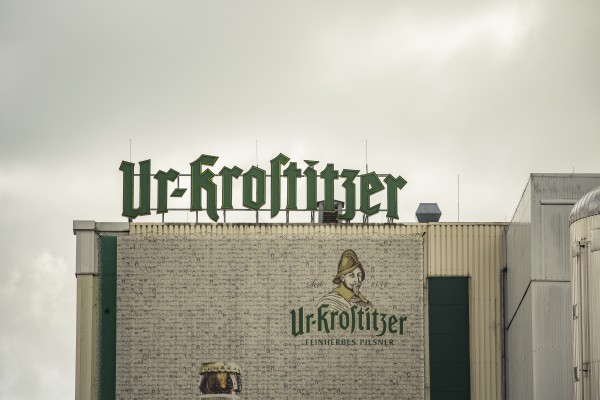 Fabrikgebäude mit großer Namensschrift und gezeichnetem Herren samt Schriftzug an der Mauer.