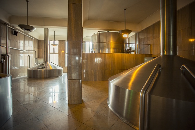 Der Innenraum einer Brauerei mit glänzenden Metalltanks und Fliesenboden.