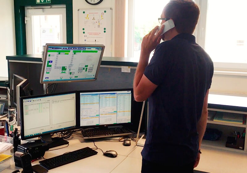 Ein Mann steht in einem Büro und telefoniert, umgeben von mehreren Computern und Bildschirmen.