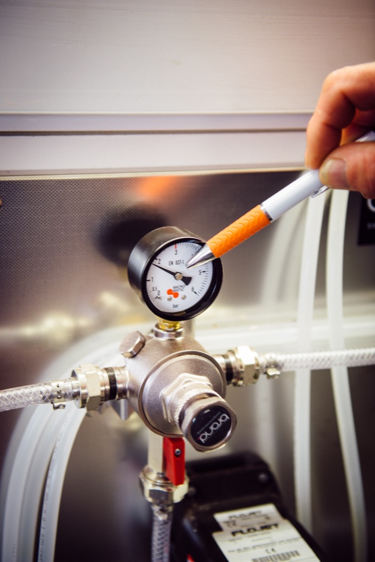 Eine Hand hält ein Messgerät an eine Apparatur mit mehreren Schläuchen und Ventilen.