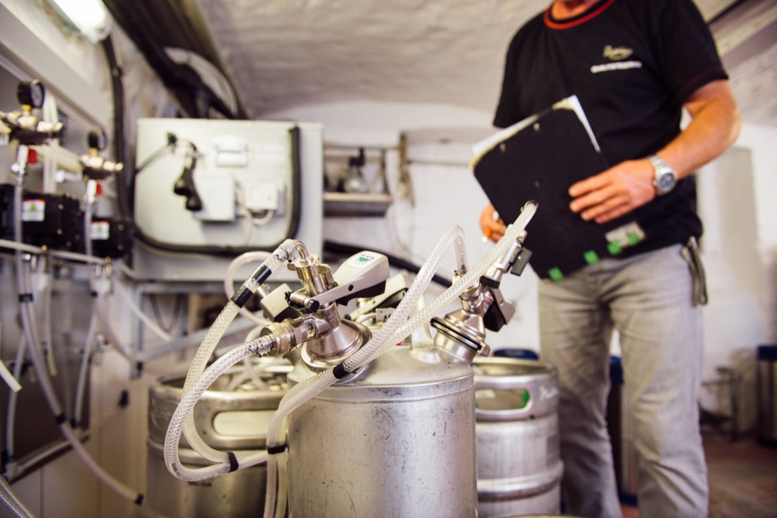 Ein Mann steht in einer Brauerei neben Metallfässern und prüft Ausrüstung.
