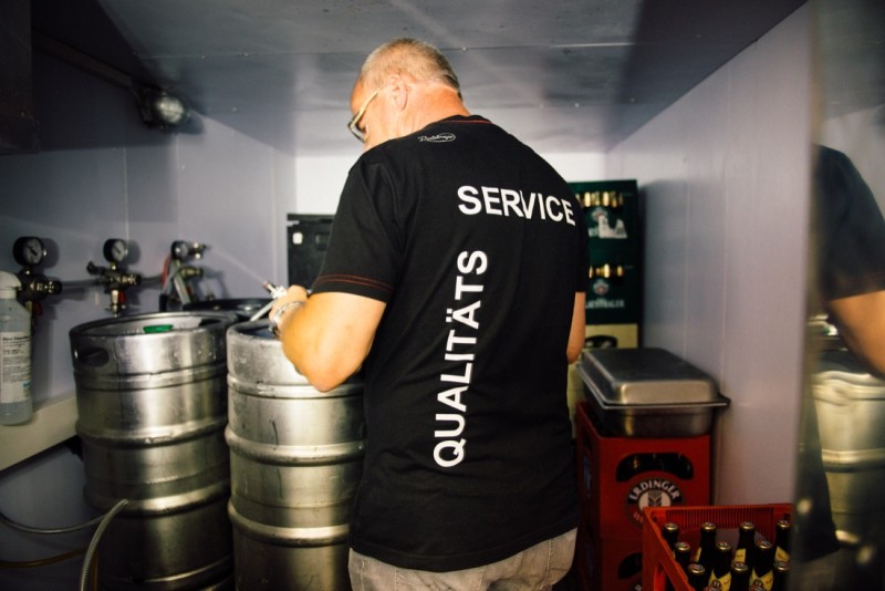 Ein Mann in einem dunklen Service-Shirt notiert etwas neben mehreren Metallfässern.