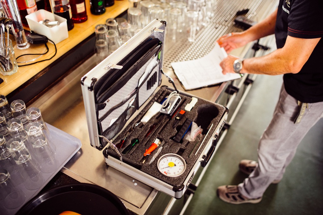 Ein Mann steht an einer Bar neben einem geöffneten Werkzeugkoffer voller Instrumente.