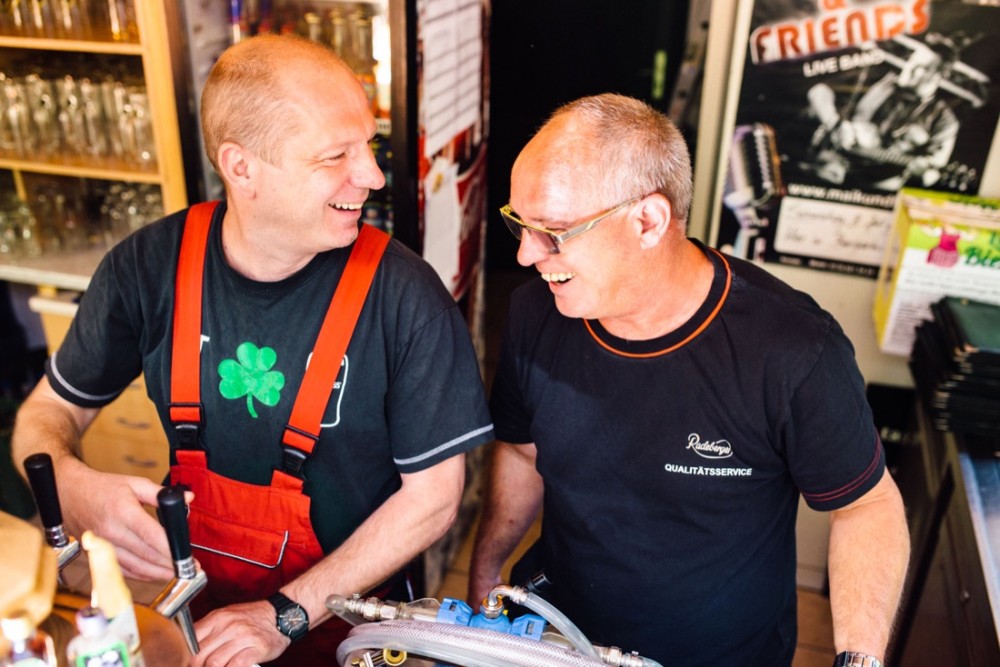 Zwei Männer lachen und unterhalten sich freundlich an einer Bar.