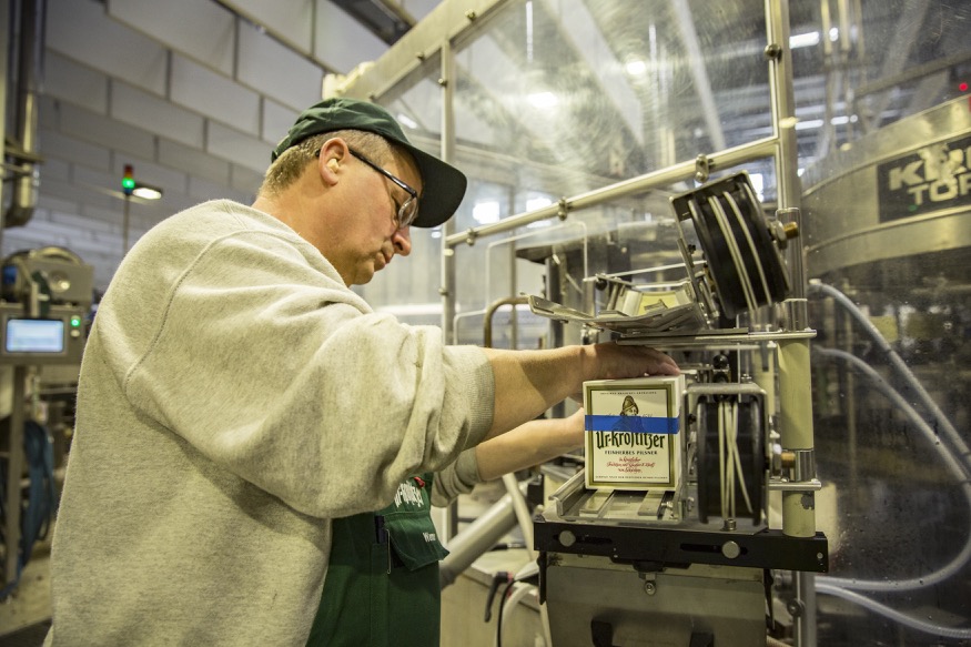 Ein Mann in Arbeitskleidung bedient eine Maschine in einer Fabrikhalle.