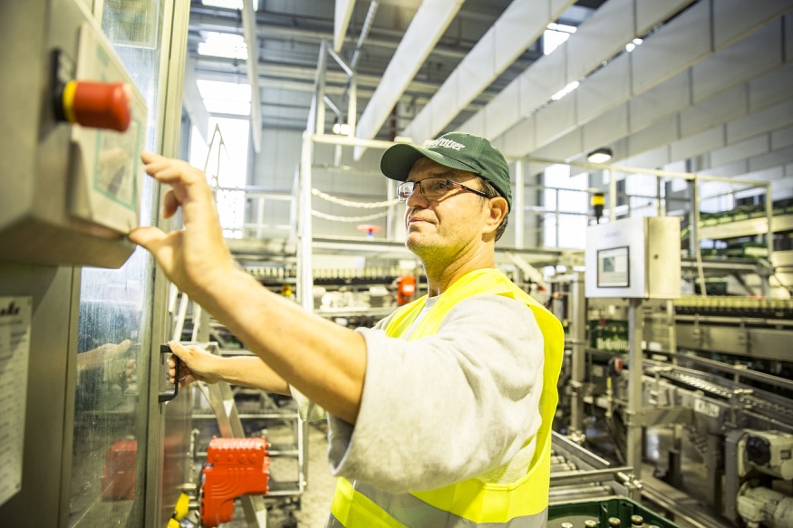 Ein Arbeiter in Sicherheitskleidung bedient eine Maschine in einer Fabrikhalle.