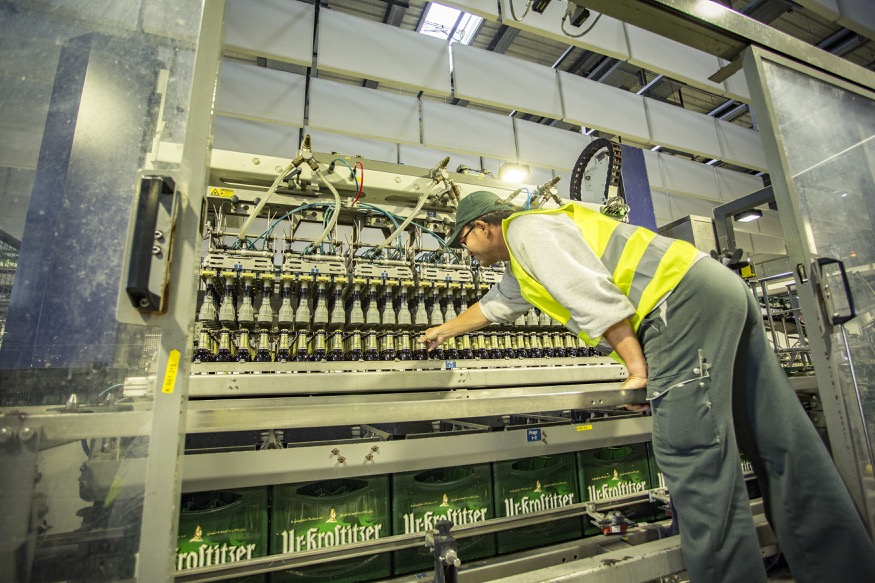 Ein Arbeiter in Schutzausrüstung überprüft Flaschen auf einem Förderband in einer Fabrik.