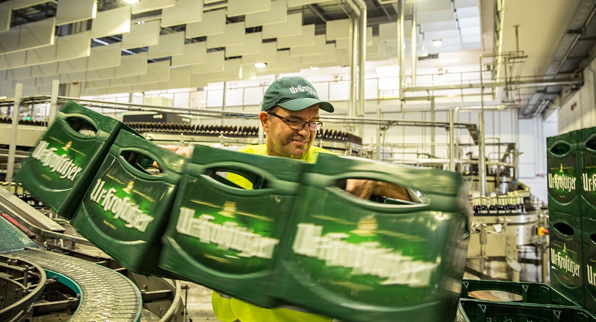 Ein Mann trägt grüne Bierkisten in einer modernen Brauerei.