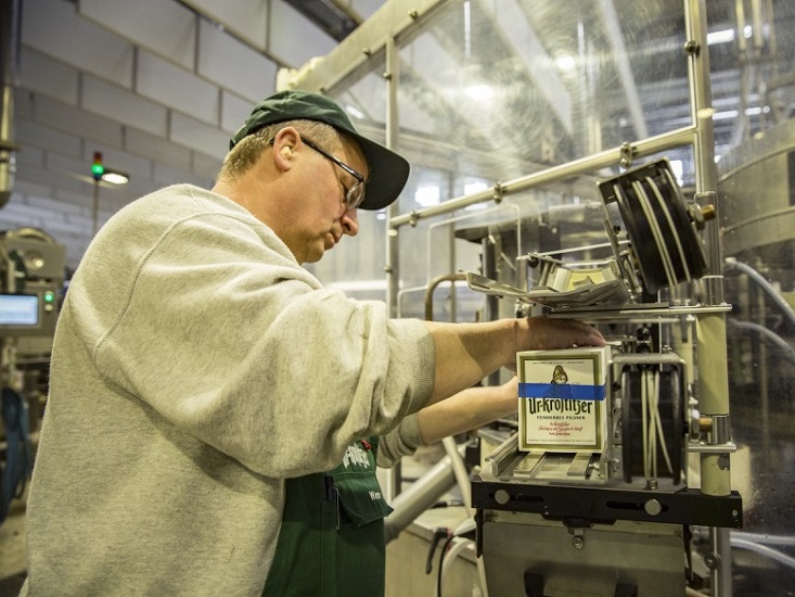 Ein Mann in Arbeitskleidung bedient eine Maschine in einer Fabrikhalle.