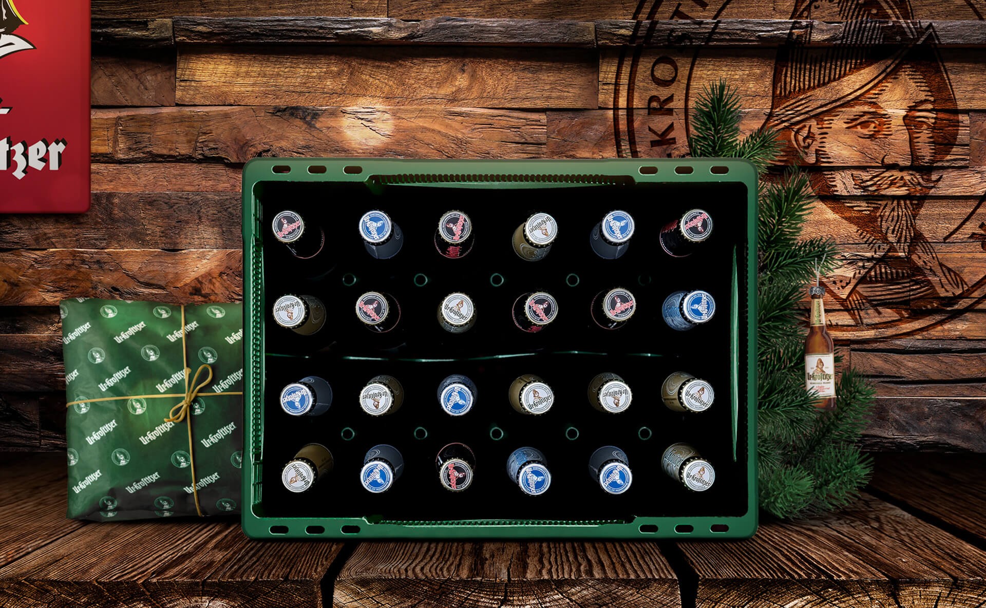 Ein grüner Getränkekühlschrank steht vor einer Holzwand und ist mit verschiedenen Bierflaschen gefüllt. Neben dem Kühlschrank liegt ein grünes Geschenk.