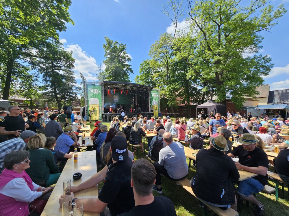 Menschen sitzen im Freien bei einem Musikfestival, umringt von Bäumen und genießen die Aufführung.