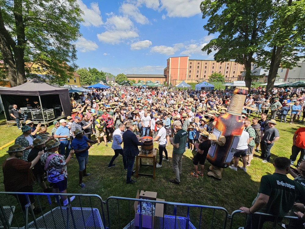 Eine Menschenmenge versammelt sich bei einem Festival im Freien, Sonnenschein und Bäume umgeben sie.