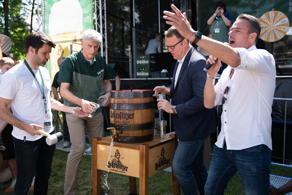 Vier Männer zapfen Bier aus einem Holzfass bei einer Veranstaltung im Freien.