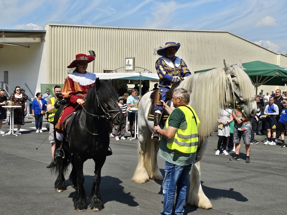 Zwei Reiter in historischen Kostümen sitzen auf ihren Pferden vor einer Menschenmenge.