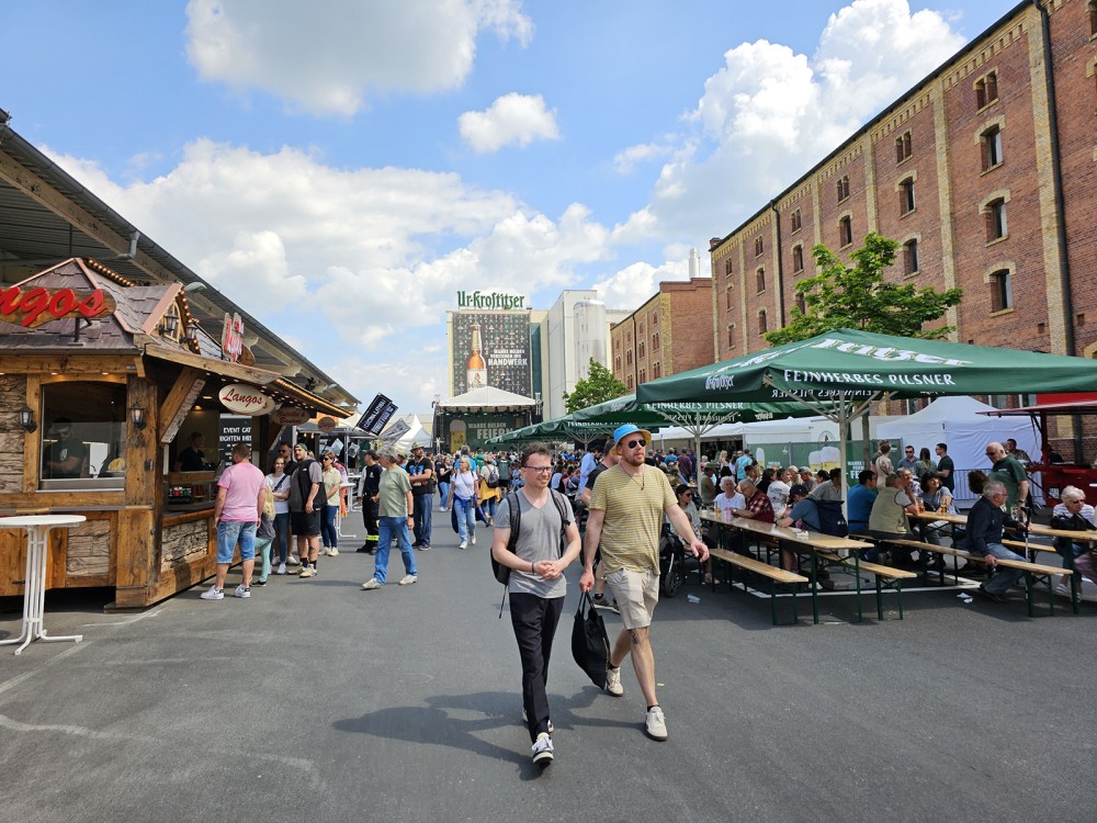 Menschen laufen und sitzen bei einem Food-Markt im Freien zwischen alten Gebäuden.