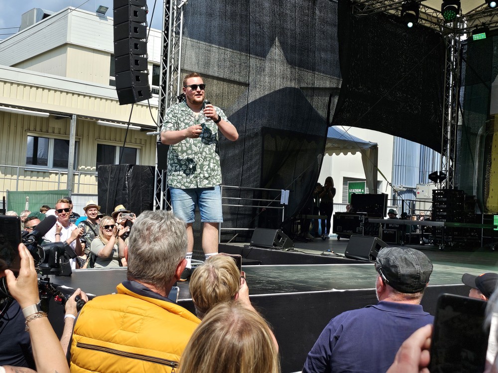 Ein Mann spricht in ein Mikrofon auf einer Bühne vor einer Menschenmenge.