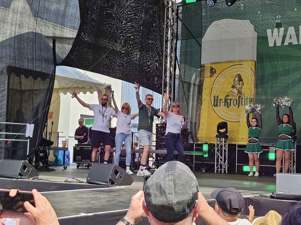 Fünf Erwachsene feiern auf einer Bühne, flankiert von vier Cheerleadern.