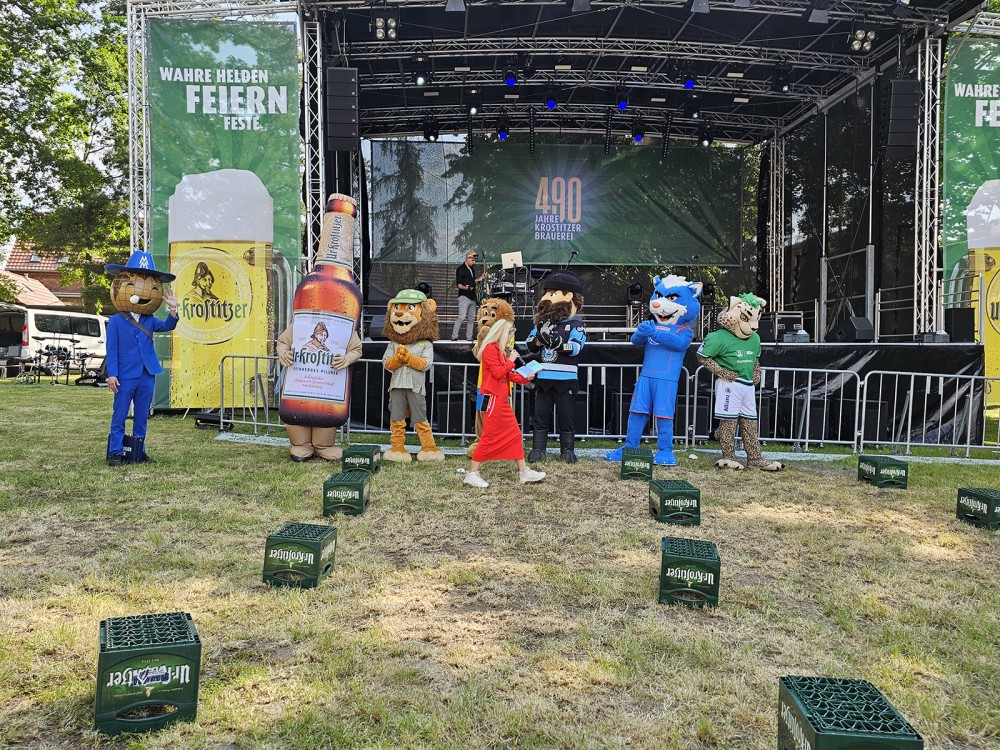 Kostümierte Maskottchen stehen vor einer Bühne auf einer Veranstaltung.