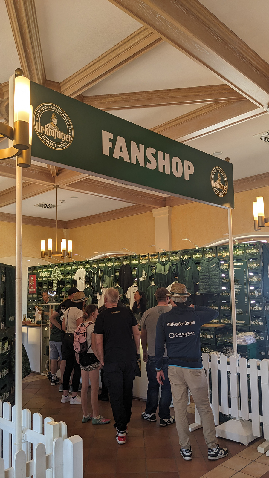 Menschen stehen in einem Fanshop mit Kleidung und Souvenirs unter einem Schild.