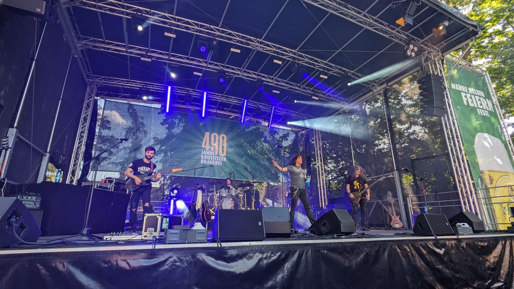 Vier Musiker performen auf einer beleuchteten Bühne vor einem Baumhintergrund.