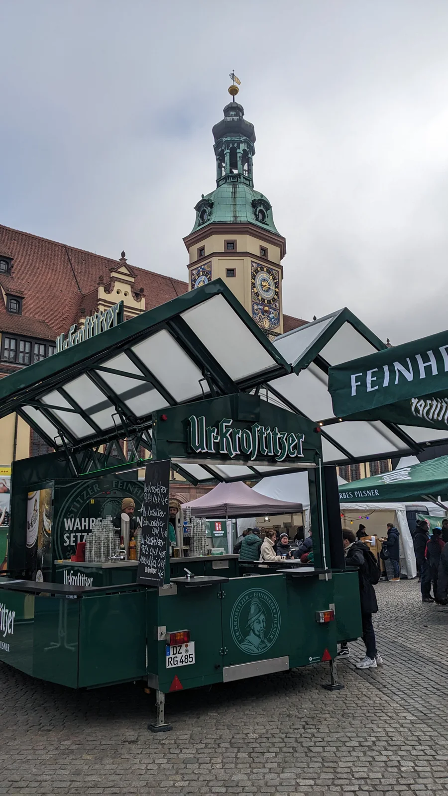 Ein Verkaufsstand für Getränke steht auf einem Platz vor einem Turm mit Uhr.