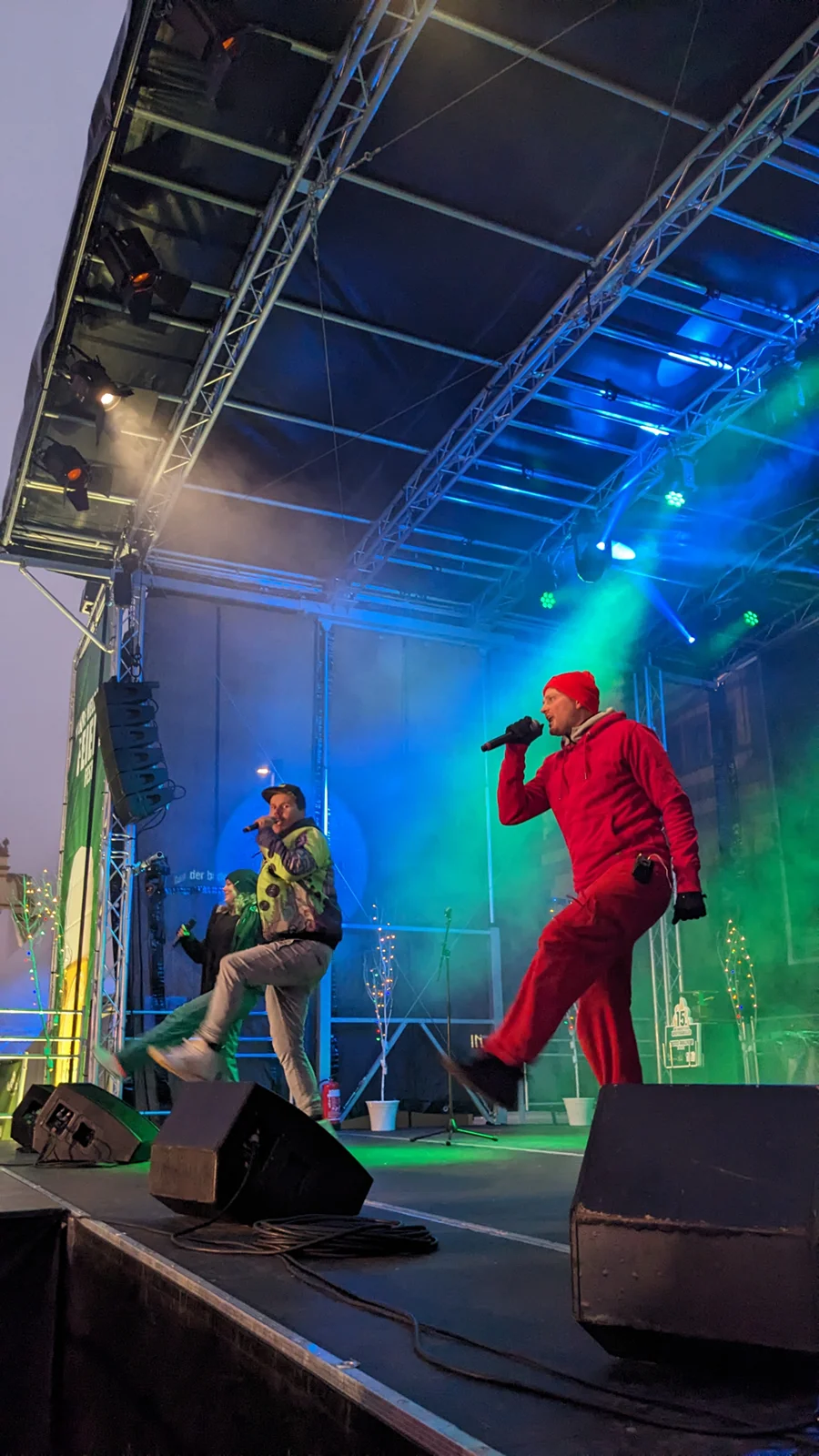 Drei Sänger performen energisch auf einer beleuchteten Bühne bei einem Konzert.