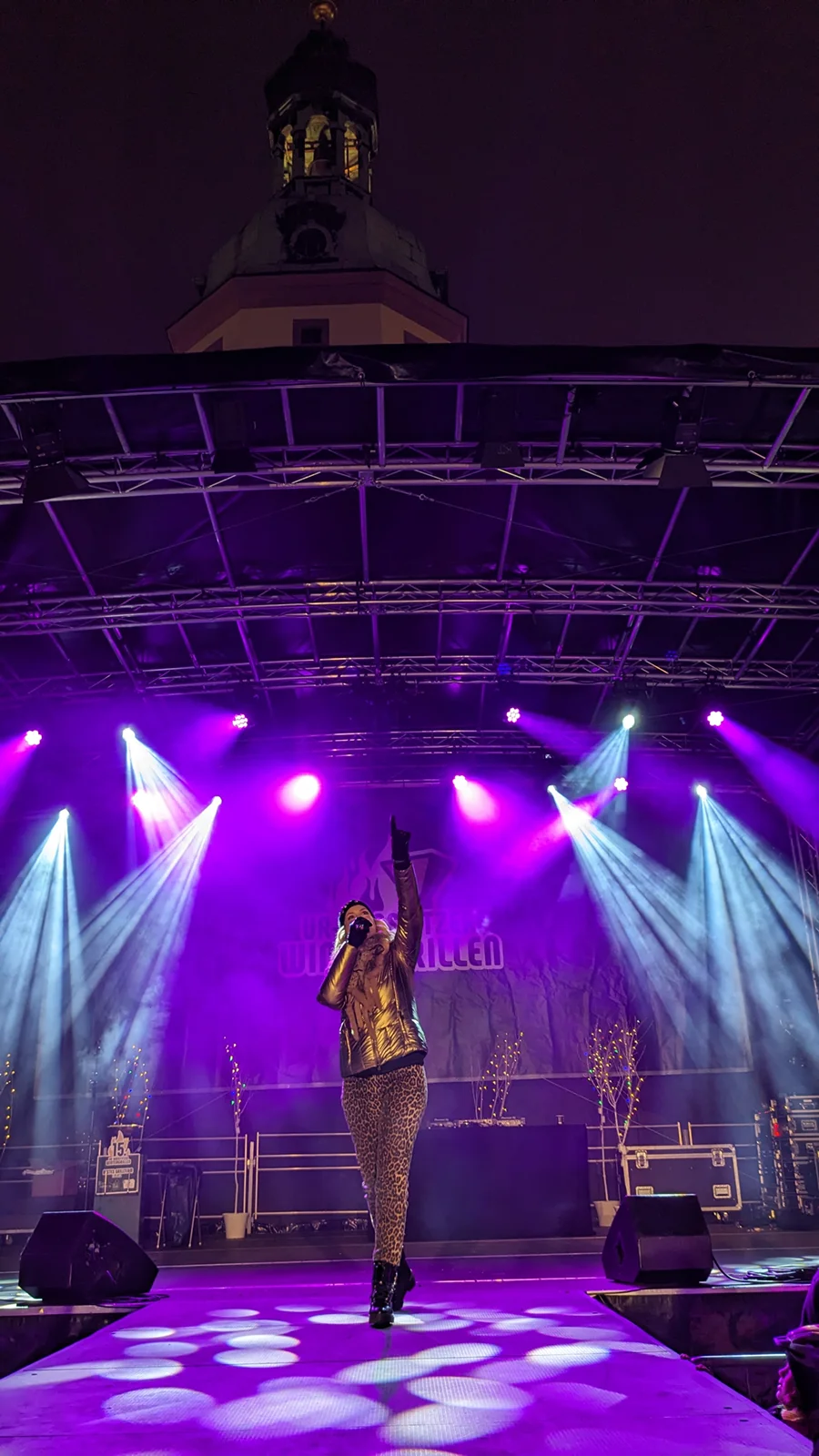 Eine Sängerin performt auf einer Bühne bei Nacht vor einer beleuchteten Kirchturmspitze.