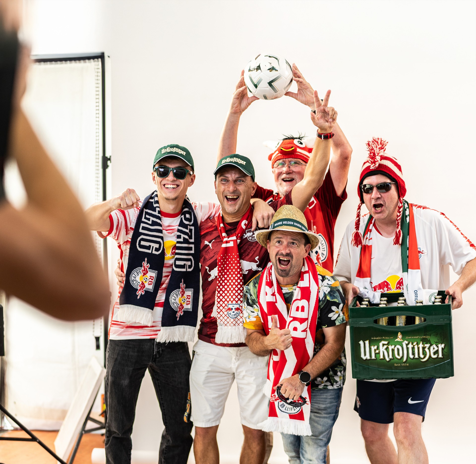 Fotoshooting einer Gruppe jubelnder Männer mit RB Leipzig-Fanartikeln und einer Kiste Ur-Krostitzer Bier.