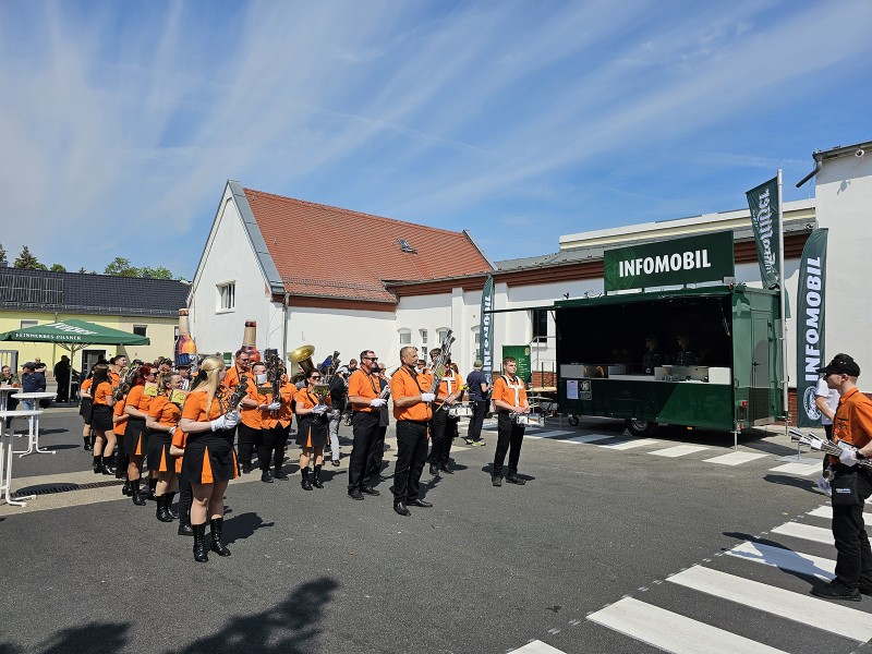 Eine Gruppe von Menschen in orangefarbenen Uniformen spielt draußen Instrumente neben einem Info-LKW.