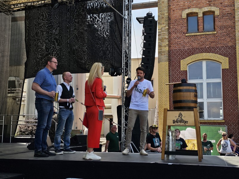 Fünf Personen stehen auf einer Bühne vor einem historischen Gebäude und sprechen.