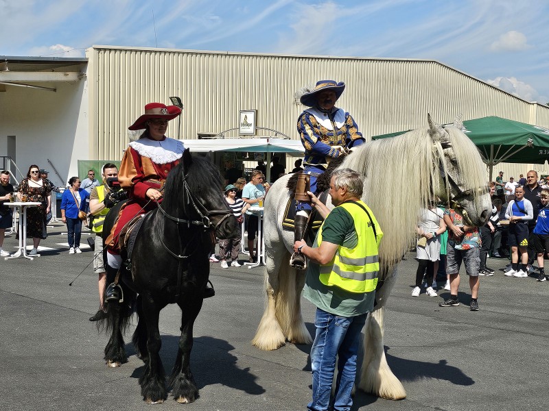 Zwei Reiter in historischen Kostümen sitzen auf ihren Pferden vor einer Menschenmenge.