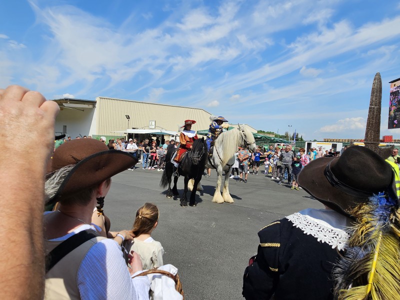 Menschen in traditioneller Kleidung reiten auf Pferden bei einer Veranstaltung.
