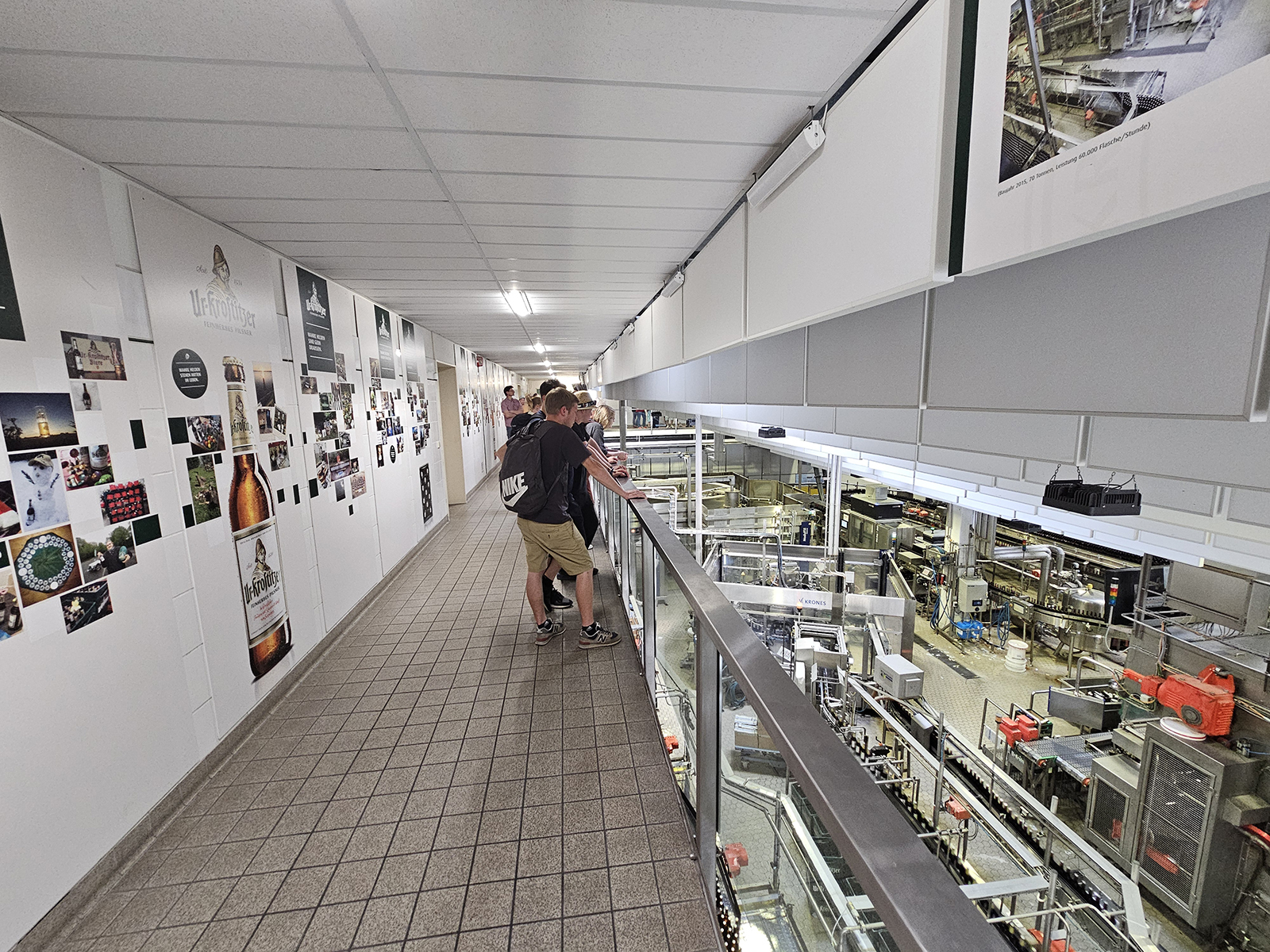 Zwei Personen betrachten Fotoausstellungen auf einer Galerie über einer Industrieanlage.