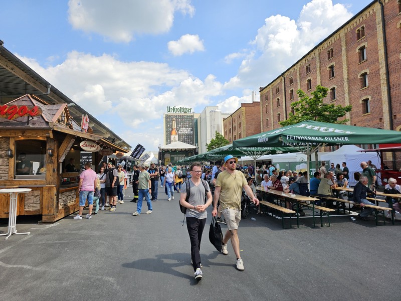 Menschen laufen und sitzen bei einem Food-Markt im Freien zwischen alten Gebäuden.