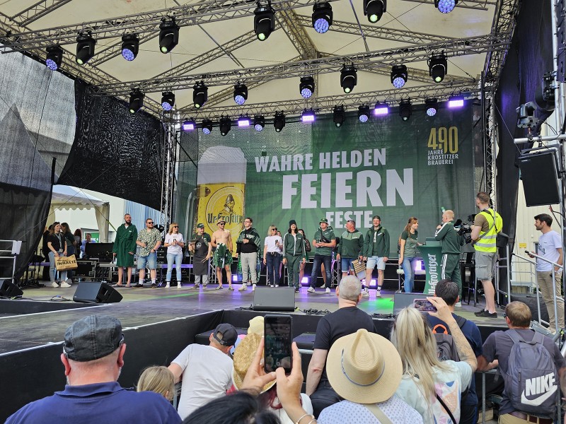 Verschiedene Personen stehen auf einer beleuchteten Bühne während eines öffentlichen Events.